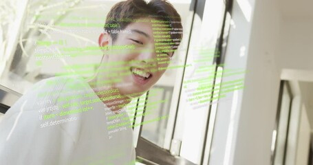 Animation of computer language over smiling asian man sitting on chair at home