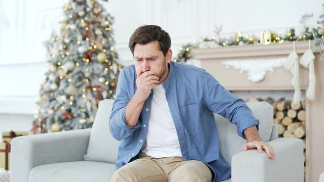 Man suffering from nausea, wants to vomit sitting on sofa in living room at home during winter New Year Christmas Xmas holidays. Unhealthy male feels bad, has a stomach ache after celebrating a party