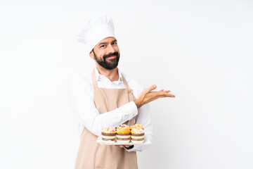 Young man holding muffin cake over isolated white background presenting an idea while looking smiling towards