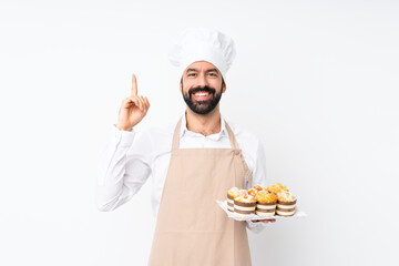Young man holding muffin cake over isolated white background pointing up a great idea