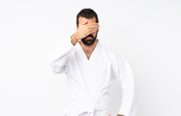 Young man doing karate over isolated white background covering eyes by hands. Do not want to see something