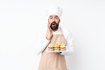 Young man holding muffin cake over isolated white background with surprise and shocked facial expression