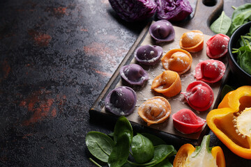 Сolored dumplings on kitchen board, pepper and basil on dark background, space for text