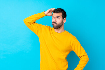 Young caucasian man over isolated blue background having doubts while scratching head