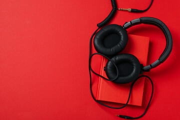 Headphones and book on red background, space for text