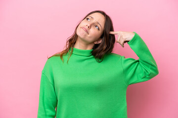 Young caucasian woman isolated on pink background making the gesture of madness putting finger on...