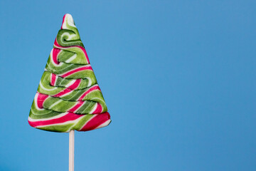 Christmas tree candy lollipop on blue background. Space for text. Christmas seasonal greetings....