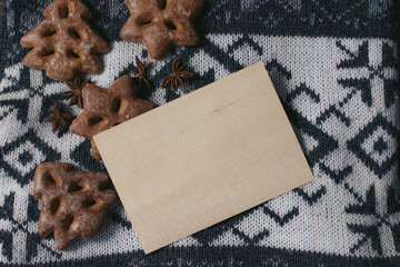 Empty wooden plate with space for text on a knit sweater featuring snowflakes with gingerbreads. Christmas holidays. New Year composition