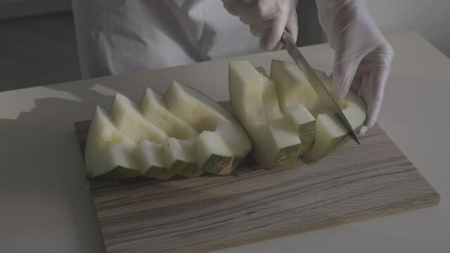 close-up of a chef's hands in protective gloves slicing a melon on a wooden board s-log video