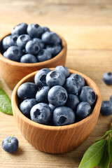 Bowls of fresh tasty blueberries on wooden table, closeup