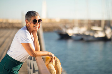 Senior woman wearing sunglasses at marina, looking at sailboats