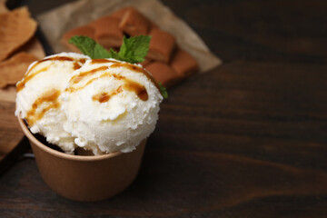 Scoops of tasty ice cream with caramel sauce and mint on wooden table, closeup. Space for text