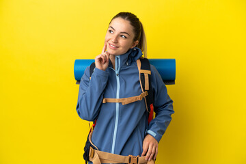 Young mountaineer woman with a big backpack over isolated yellow background thinking an idea while looking up