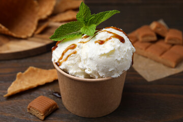 Scoops of tasty ice cream with caramel sauce, mint leaves and candies on wooden table, closeup