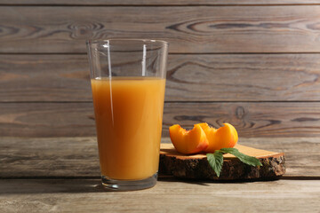 Glass of delicious peach juice, cut fresh fruit and leaves on wooden table