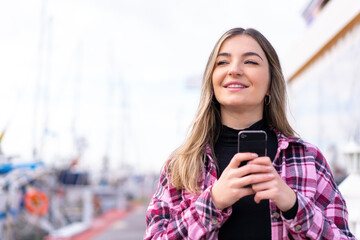 Young pretty Romanian woman at outdoors using mobile phone and looking up