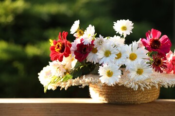 Beautiful wild flowers in wicker basket on wooden table against blurred background
