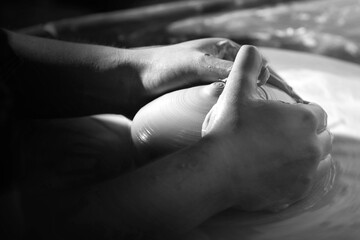 Black and white image of the hands of a young female potter throwing plates on a spinning wheel. Blurring to show motion.