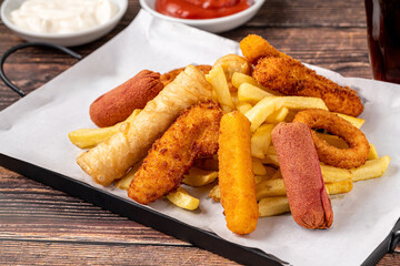 Snack plate with french fries, crispy chicken, cheese sticks, sausage and spring rolls on wooden table