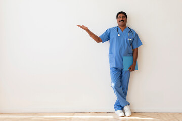 Portrait Of Indian Male Doctor Wearing Uniform Pointing Aside At Copy Space