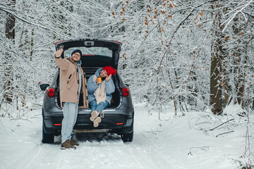 A happy couple takes a selfie in the car in a snowy forest, they stopped to rest