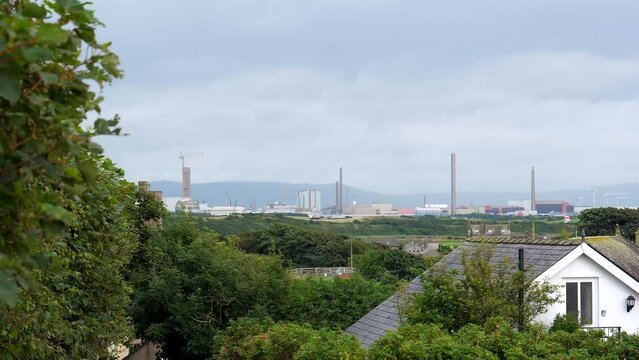 Closed nuclear power station site in Sellafield through rooftops on overcast day, handheld shot.
