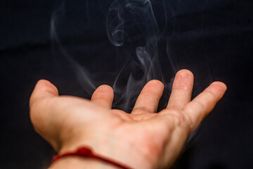 gray smoke comes with beautiful shapes in the air from a male hand on a black background	
