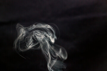 A lot of white smoke from incense flies beautifully in the air on a black background	
