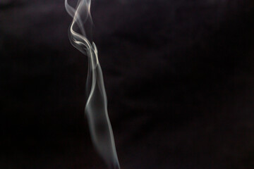 White smoke from incense curls beautifully up in the air against a dark background	
