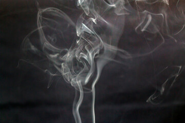 A lot of incense smoke swirls in on a dark gray background creating shapes	
