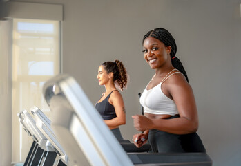 Fototapeta premium African woman jogging in indoor fitness active young woman running on treadmill at the gym exercising. Run on a machine.