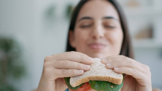 Video of  beautiful sporty woman eating healthy sanwich while looking at camera in the kitchen at home