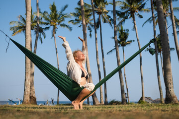 A young girl with curly blond hair lies in a hammock in nature and enjoys life, in the foreground her bare foot.