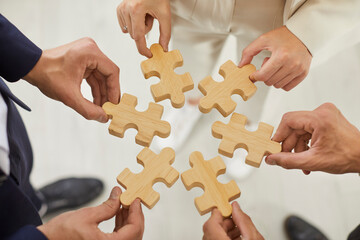 Top view cropped hands of a group of business people assembling wooden puzzle. Coworkers join...