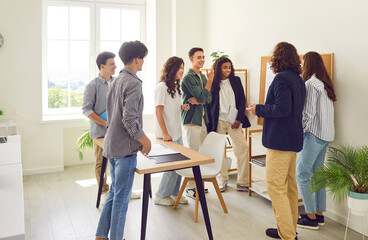 Young male teacher standing in a circle with college or high school students, talking and showing...