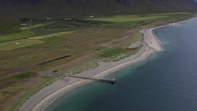 Aerial flyover white sandy beach with jetty and ocean water beside green scenery on Iceland - Wide shot