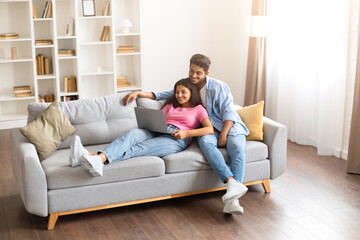 Obraz premium Indian couple relaxing on sofa with laptop, sharing a moment