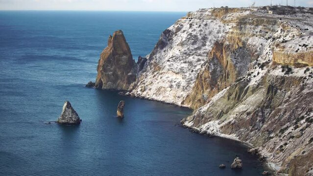 Snow covered rocky cliffs over sea. Winter landscape over the sea bay. Juniper tree under snow. Concept of winter holidays, travel and recreation. Cape Fiolent in Balaklava, Sevastopol, Crimea