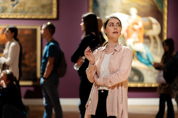 Portrait of young amazing Caucasian woman holds glasses and looking at exhibition. People and...