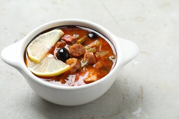 Meat solyanka soup with sausages, olives and vegetables in bowl on white textured table. Space for text