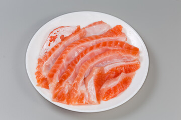 Salted slices of salmon bellies on dish on gray background
