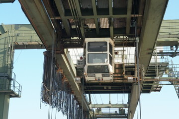 White cabin of green gantry crane operated by stevedores in Houston container terminal. There is upper part of construction of machinery and various cables.