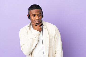 Obraz premium Telemarketer latin man working with a headset isolated on purple background looking to the side and smiling
