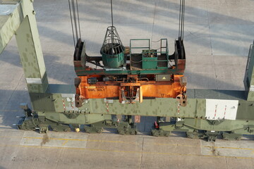 Orange spreader of green gantry crane on rails using for loading and discharging of containers from cargo ships in Houston Terminal operated by stevedores.