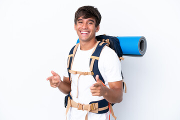 Young mountaineer woman with a big backpack over isolated white background pointing to the front and smiling