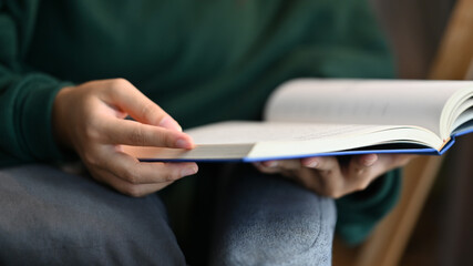 Cropped shot of young woman sitting on couch at home in living room, reading literature - obrazy, fototapety, plakaty