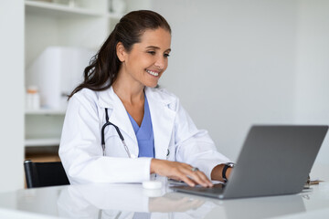 Mature doctor using laptop at clinic, telemedicine concept - obrazy, fototapety, plakaty