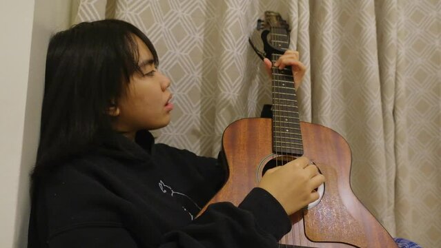Attractive filipino girl strumming acoustic guitar and jamming. Static medium