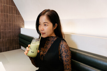 Asian woman with ice matcha in hand at cafe looking healthy