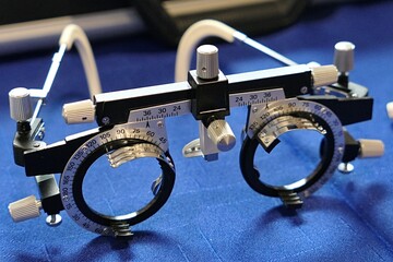 Left front view of steel trial optometrist and ophtalmology frame for examination of eye refraction errors, with massive position adjustment screws, displayed on blue fabric.  